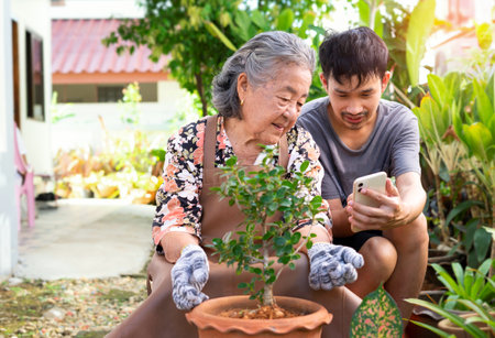 adult grandson showing grandma a smartphone, a variety of planting ornamental.concept of family activity at homeの写真素材