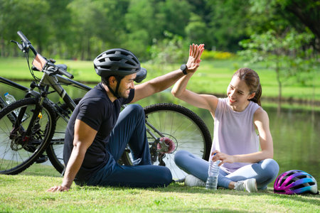 young asian couple hands high five together while resting beside the pond in the park, happy family...