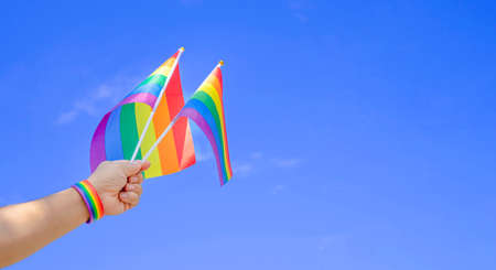 man hand wearing lgbt rainbow wristband and waving rainbow flags on blue sky with copy space, concept for lgbtq happy pride monthの写真素材