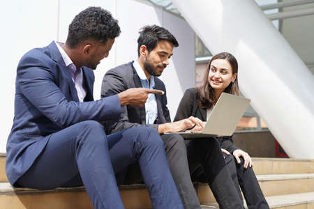 multiracial business people in suit working with laptop on site outdoors, young happy businessman and businesswoman discuss work outside buildingの写真素材