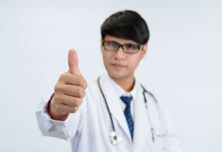 young asian doctor showing hand thumb up,selective focus at hand, isolated on blue background. concept of hand gesture sign for good,excellent,agree,approval, going according to plan etcの写真素材