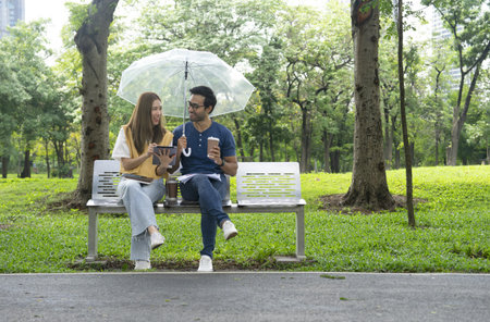 attractive asian couple sitting and chatting happily in the park, young couple working casually with...