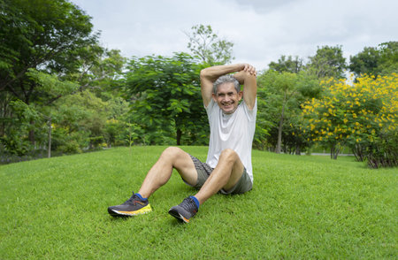 happy senior man sitting on lawn and cooling down after workout, older adult resting in the park...