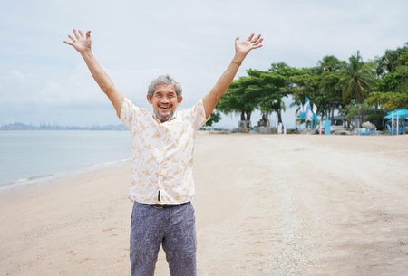 happy senior enjoying the summer vacation, old mature man standing and outstretched arms feeling free at the beachの写真素材