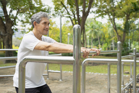 happy senior man with grey hair doing exercise on outdoor fitness equipment in the city park