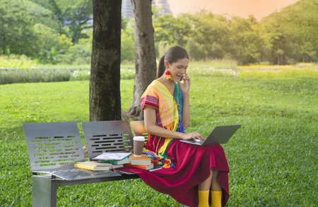 woman transgender in colorful rainbow dresses sitting on bench in the park, the lgbtq transgender is typing laptop computer and using smartphone. concept lgbtq lifestyle, lgbtq pride monthの写真素材