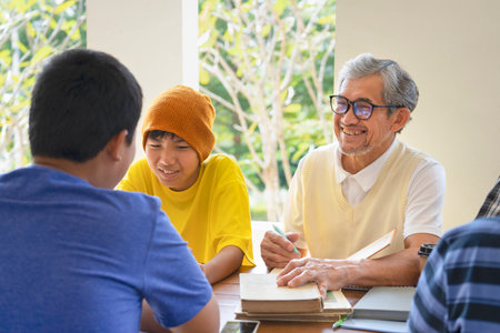 adult older teacher helping teenagers students to do homework or report, children having fun while doing homework with teacherの写真素材