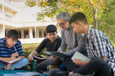 senior man teacher and group of teenager boys sitting together at school backyard, a teacher holding a book explaining a lesson to the students, concept of education,
learning casual outdoors ,helping,tutoringの写真素材