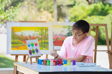asian teenager boy wears eyeglasses thinking about comparison of primary colors while painting watercolor, drawing makes teens express their feelings and spark their creativityの写真素材