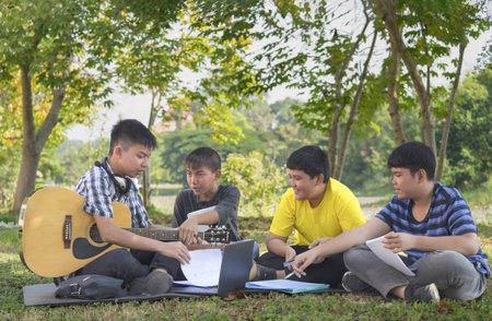 teen boy holding guitar,helping his three school junior boys to play and compose music,happy asian teenagers playing music together,concept for teenagers adult helping junior to do school arts projectの写真素材