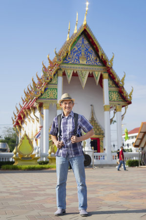portrait asian senior man wears hat and carry backpack standing in front of temple in Thailand, happy elderly pensioner male travelling cultural attractions destinationの写真素材