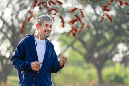 portrait happy senior man with grey hair and beard  in sportswear exercising in the park during sunriseの写真素材