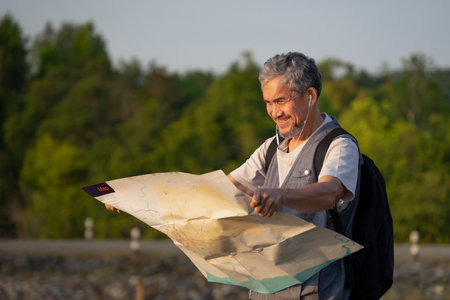 senior man tourist wears headphones to listen music,find a location on the map for camping on summer holiday trip by the damの写真素材