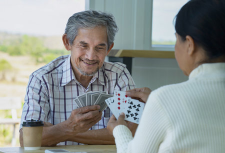 happy senior couple enjoy playing cards game together, concept elderly pensioner lifestyle, entertainment, recreation, encourages social interaction, help memory retentionの写真素材