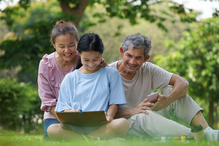 grandparents and granddaughter enjoy leisure time together at the park, grandchild painting a picture,grandfather and grandmother smile look at her, concept of family lifestyle,relationship,activities,holidaysの写真素材