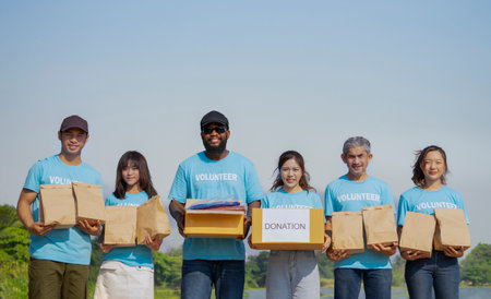 portrait diverse of people in volunteer blue t-shirt holding donation box and donated items standing in the park or donation area, group of volunteers working by the pondの写真素材