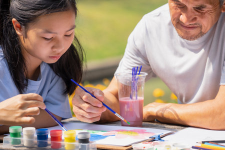 asian teenage girl painting watercolors with her grandfather, happy family granddaughter and grandfather spend leisure time together in the garden, concept family lifestyle, relationship,the love of a familyの写真素材