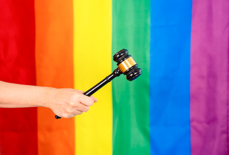 hand of gay pride holding wood gavel or judge hammer background lgbtq rainbow flag,concept for lgbt gender diversity claim justice rights of amendment,law,discrimination,equality of lgbtq communityの写真素材
