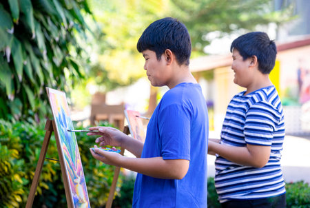 happy asian teenage boys painting on canvas,talking,laughter joyfully at outdoors school art club,teens activities,hobby,talent,drawing makes teens express their feelings and spark their creativityの写真素材