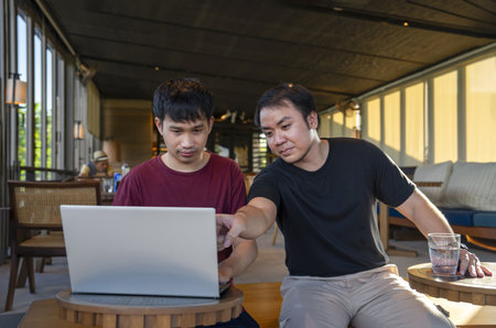 young asian man working remotely on internet online over laptop on vacation while take a break with his friend in cafe on mountain, destination in Thailand.concept of travel freely,digital nomadの写真素材