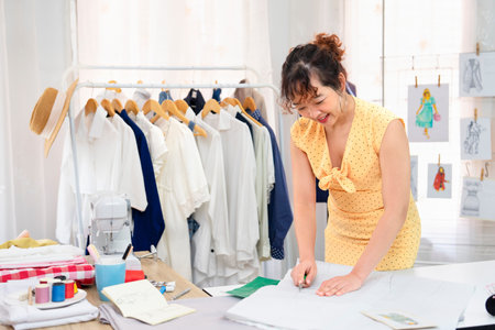 beautiful young asian female working in fashion studio, a smiling experienced tailor is tailoring...
