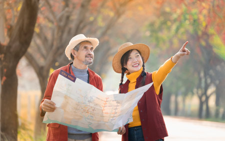 A senior man holding paper map talking with young adult daughter while she is pointing index to the location direction,happy moment of father and daughter spend holiday time in autumn travel togetherの写真素材
