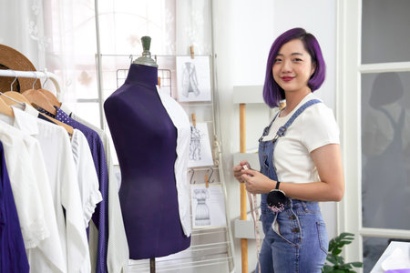 portrait young cool asian female clothing designer with purple color hair working with mannequin at her modern fashion studio,concept of fashion design.dressmaking,tailoring,business,industryの写真素材