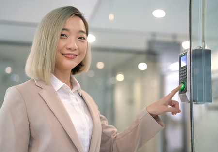 A smiling young female employee using index finger press sensor for record time attendance - out work at the companyの写真素材