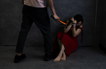 woman afraid in red being tied, psycho killer man holding hammer threatening to female victim,concept of women victim,hostage,crime,violenceの写真素材