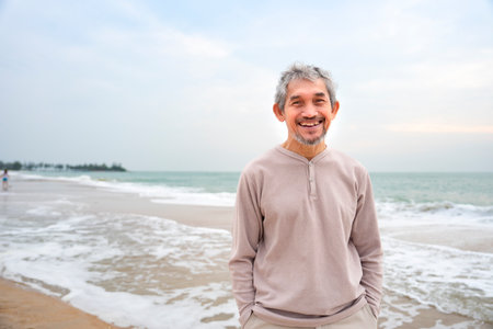 portrait asian senior male smiling and standing in nature,happy mature man enjoy summer time on the beach,concept of elderly pensioner lifestyle,holiday,travel,wellness,wellbeingの写真素材