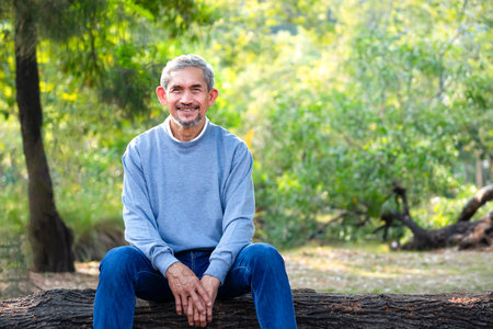 portrait mature man spend leisure time sitting on a log in the forest park,asian senior man smiling...