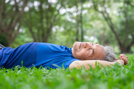 sporty senior man lying down on grassess and taking a nap while resting in park,adequate sleep during the day help elderly body to rest and restore strength to help carry out daily activities normallyの写真素材
