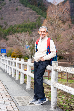 portrait asian senior man with grey hair in sweater carry backpack walking in the city, destination tourist attraction in Japanの写真素材