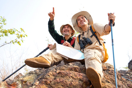 active father and adult son successfully climbed up on the top of a mountain,sitting,relax,senior man father pointing index to something and laughing together,family relationship,adventure in natureの写真素材