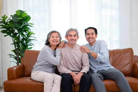 portrait senior couple with middle aged male, asian family sitting on sofa in the living room at...