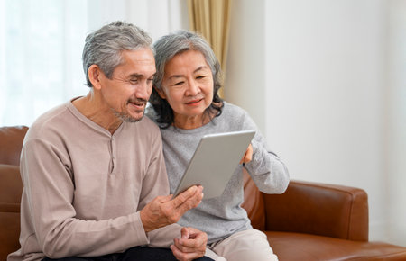 cheerful asian senior couple spend leisure time in living room together ,exciting while surfing online on their tablet computer,concept of elderly people modern lifestyle,internet,technologyの写真素材