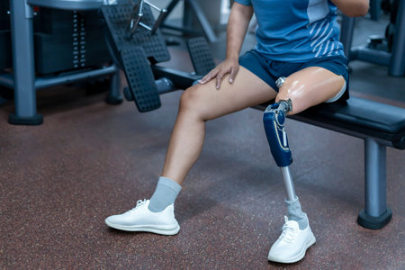 A person with prosthetic leg sitting on exercise equipment at gym,athletic woman working in fitness...