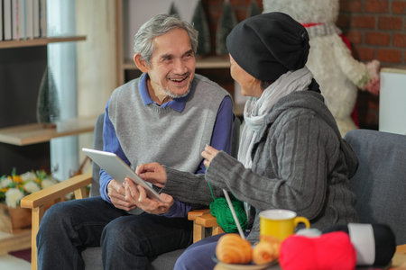 happy senior couple sitting on couch in the living room,a woman knitting with a man holding digital...