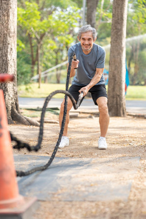 healthy senior man doing battle ropes exercise in the park,older adult athlete people workout training with outdoors gym equipment
