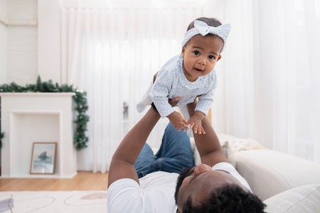 cozy black father playing with baby,lying on couch and lifting up a daughter in the living room,family lifestyle,bonding,domestic lifeの写真素材