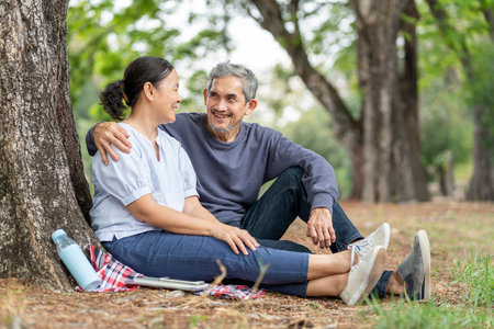 portrait bonding asian senior couple relaxing in the summer park,sitting,resting under a tree talking togetherの写真素材