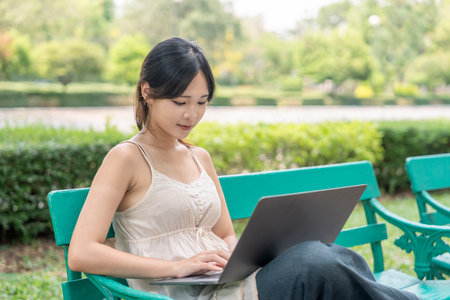 young pretty woman using laptop,sitting on bench in the parkの写真素材