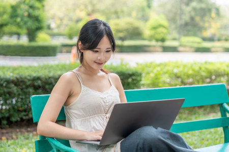 young pretty woman using laptop,sitting on bench in the parkの写真素材