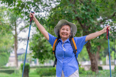 portrait cheerful senior woman wears hat,with backpack and trekking poles standing in nature,elderly asian female happy in hiking tripの写真素材