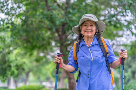 portrait cheerful senior woman wears hat,with backpack and trekking poles standing in nature,elderly asian female happy in hiking tripの写真素材