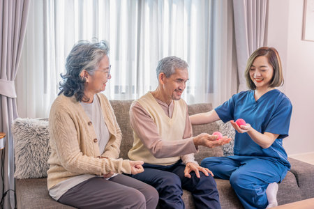 A cheerful therapist in uniform training elderly couple to stretch hands muscles with a...