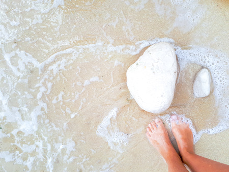 Tanned female feet in clear sea water next to white stones.の写真素材
