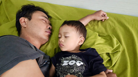 father and son sleeping together in bed, father hugging his son with warm affection, daily routine activitiesの写真素材