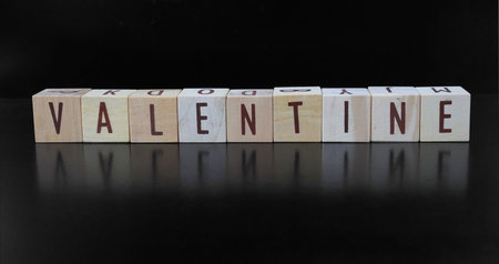 The word VALENTINE is made of letters formed from wooden blocks, isolated on a black background.