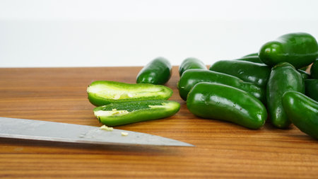 Several fresh green jalapeno peppers, one of which is open with detailed seeds, on a brown wooden cutting board, isolated on a white backgroundの写真素材